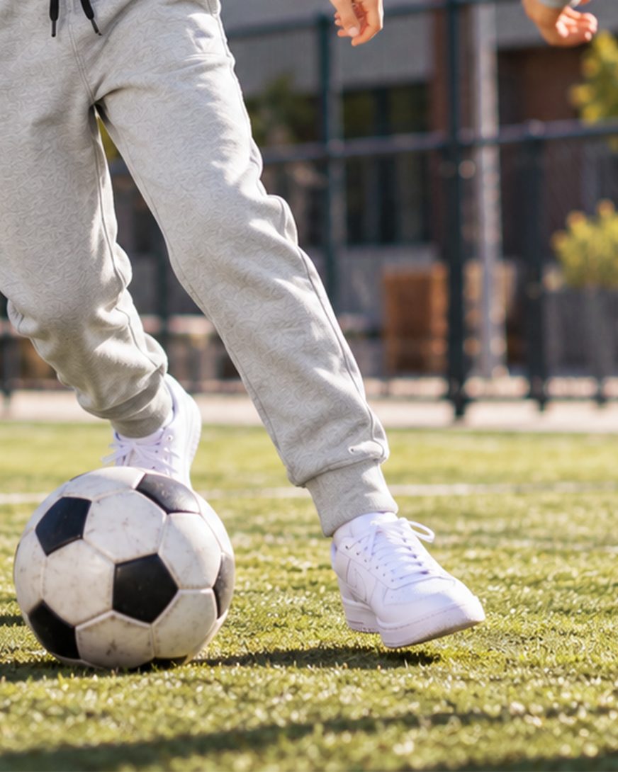 Gray joggers in motion, kicking a soccer ball on grass